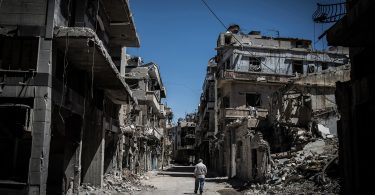 A Syrian refugee walks among severely damaged buildings in downtown Homs, Syria in 2014 (Pan Chaoyue/Flickr/CC BY-NC-ND 2.0)