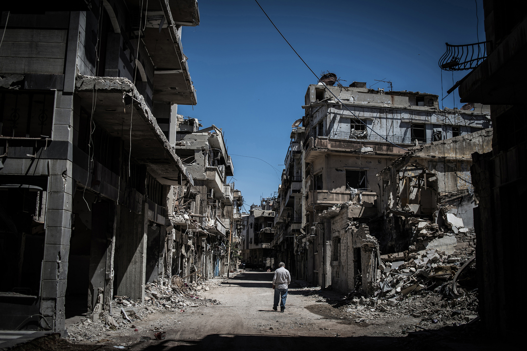 A Syrian refugee walks among severely damaged buildings in downtown Homs, Syria in 2014 (Pan Chaoyue/Flickr/CC BY-NC-ND 2.0)