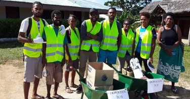 Photograph of group of eight ni-Vanuatu people in hi-vis vests with two wheelbarrows that have signs saying 'Donation TCH'.