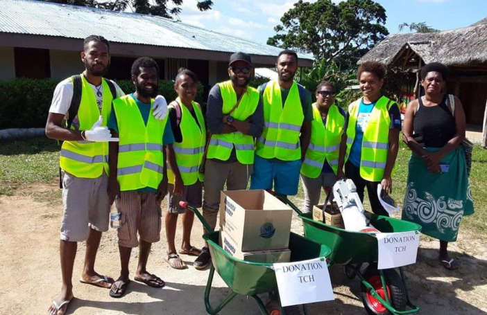 Photograph of group of eight ni-Vanuatu people in hi-vis vests with two wheelbarrows that have signs saying 'Donation TCH'.