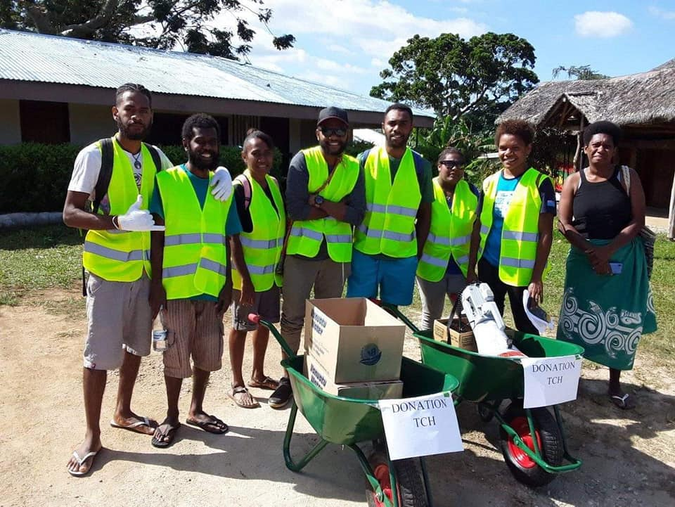 Photograph of group of eight ni-Vanuatu people in hi-vis vests with two wheelbarrows that have signs saying 'Donation TCH'.