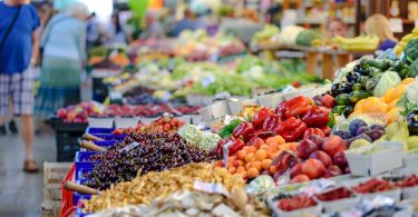 Photograph of a colourful display of fruits and vegetables in a store, including cherries, apricots, capsicums, plums, eggplant and broccoli.
