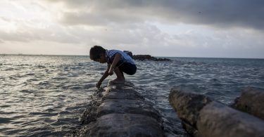 A boy plays on a flooded sea wall in Kiribati (Conor Ashleigh-World Bank)