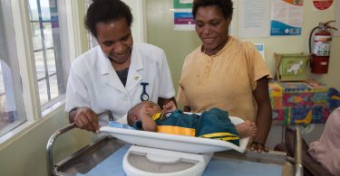 Photograph of a mother and nurse weighing a baby at a health clinic in Port Moresby, PNG