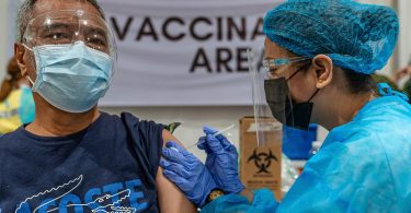 Photograph of a Philippines health practitioner giving a COVID-19 vaccination. Both people are masked.