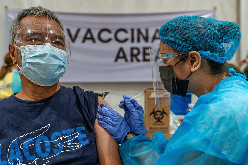 Photograph of a Philippines health practitioner giving a COVID-19 vaccination. Both people are masked.