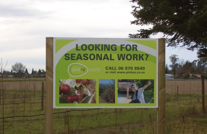 Photography of roadside sign in a field that reads 'Looking for seasonal work?'