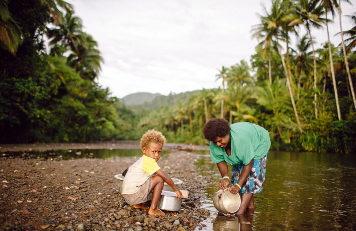 A woman cleans her pots in a river while her child watches