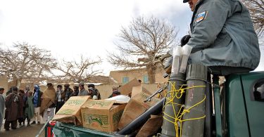Afghan National Police officer stands watch over food before distributing it to families