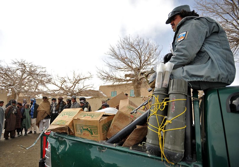 Afghan National Police officer stands watch over food before distributing it to families