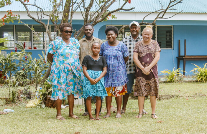 A group of six people stand outside a house.