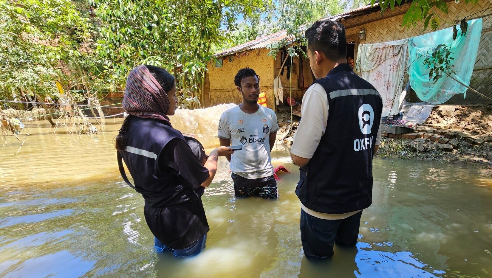 Members of Oxfam Bangladesh's Emergency Response Team talking with Rubayet in front of his damaged home